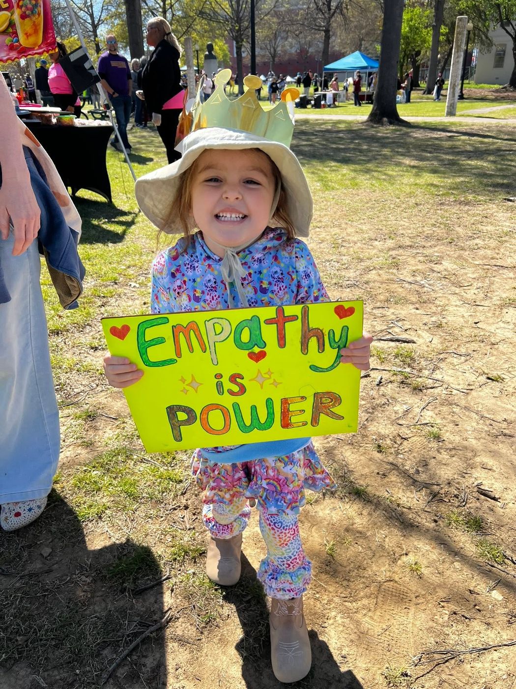 A young child in a paper crown holds a hand-lettered sign reading "Empathy is Power".