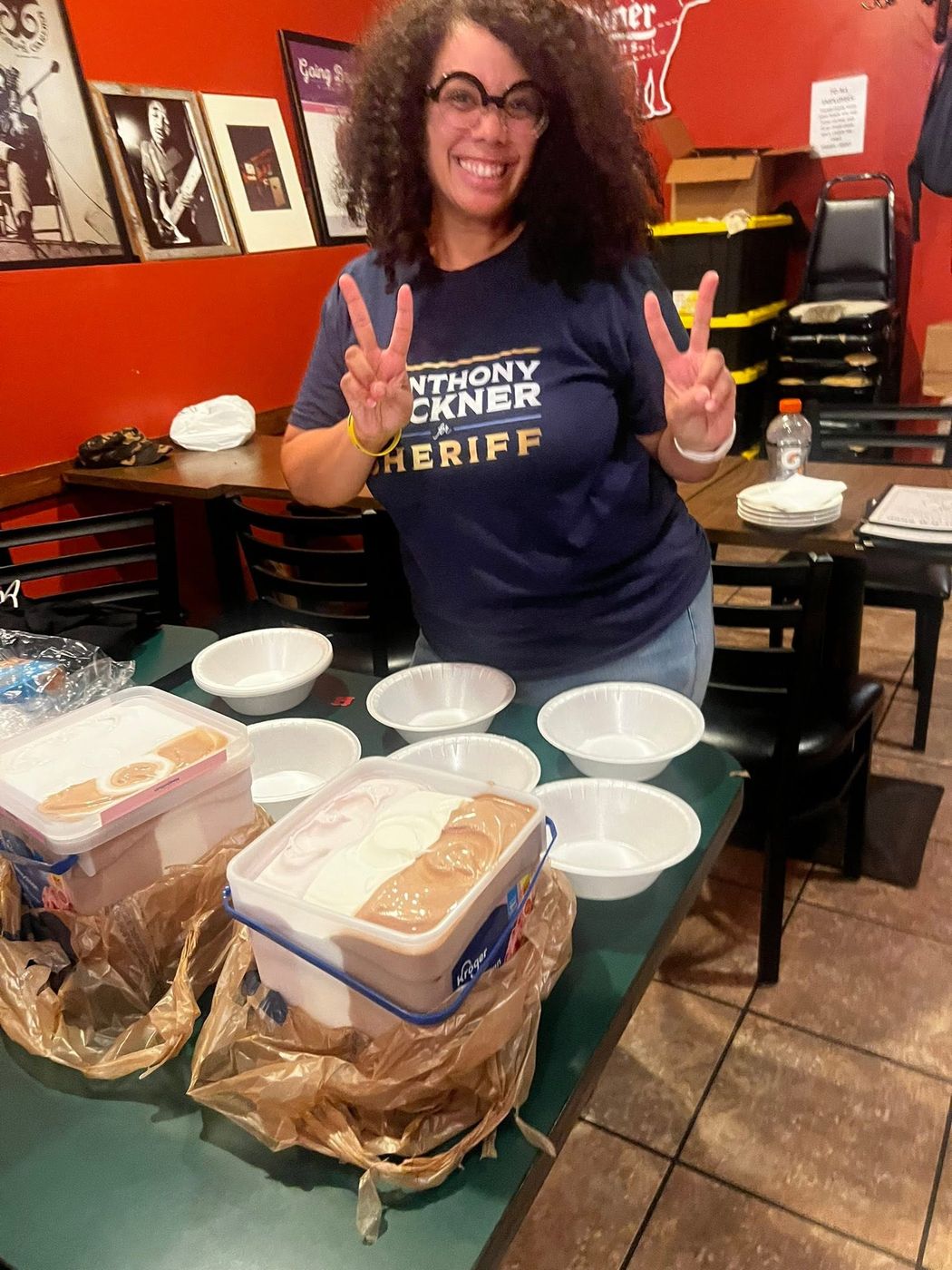 A volunteer smiling behind trays of food prepared for a club event.